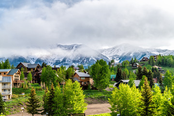 Mount Crested Butte, USA Colorado village in summer with cloudy fog mist sunrise morning and houses on hills with green trees