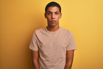 Young handsome arab man wearing striped t-shirt standing over isolated yellow background Relaxed with serious expression on face. Simple and natural looking at the camera.