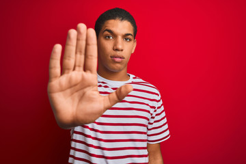 Young handsome arab man wearing striped t-shirt over isolated red background doing stop sing with...