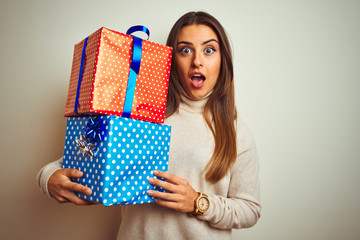 Young beautiful woman holding birthday gifts standing over isolated white background scared in shock with a surprise face, afraid and excited with fear expression
