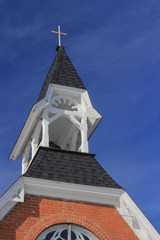 Cross sitting on a white steeple with a blue sky.