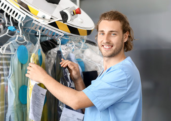 Worker of modern dry-cleaner's near rack with clothes