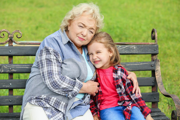 Fototapeta na wymiar Cute little girl with grandmother sitting on bench in park