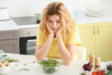 Reluctant woman with healthy vegetable salad in kitchen