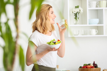 Woman with healthy vegetable salad and glass of water in kitchen