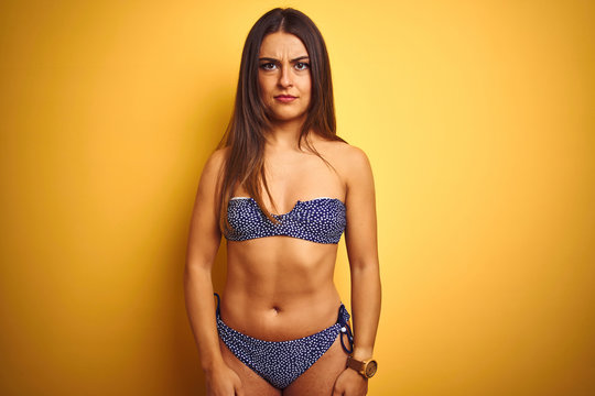 Young beautiful woman on vacation wearing bikini standing over isolated yellow background skeptic and nervous, frowning upset because of problem. Negative person.