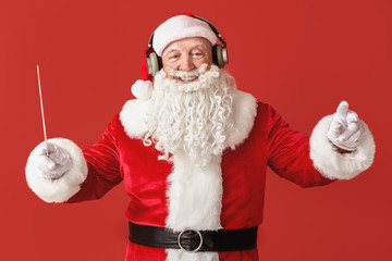 Portrait of Santa Claus with wand listening to music on color background