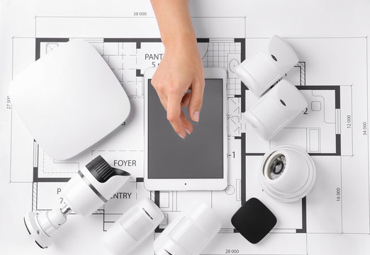 Female hand with tablet computer and different equipment of security system on home plan