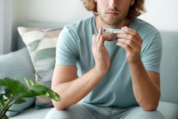 Diabetic man taking blood sample with lancet pen at home