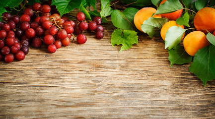 Fresh ripe red grapes and apricots on a wooden background, copy space