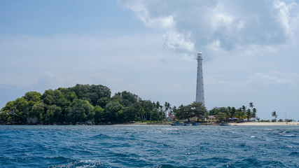 white lighthouse on the island with blue sea, big rocks and green trees