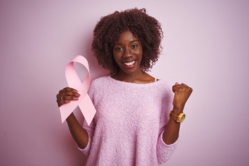 Young african afro woman holding cancer ribbon standing over isolated pink background screaming...