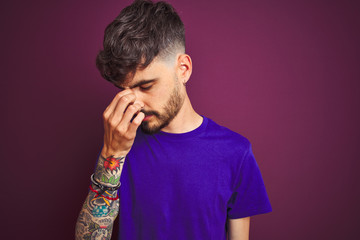 Young man with tattoo wearing t-shirt standing over isolated purple background tired rubbing nose and eyes feeling fatigue and headache. Stress and frustration concept.