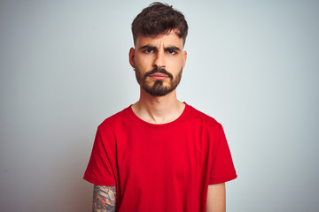 Young man with tattoo wearing red t-shirt standing over isolated white background skeptic and nervous, frowning upset because of problem. Negative person.