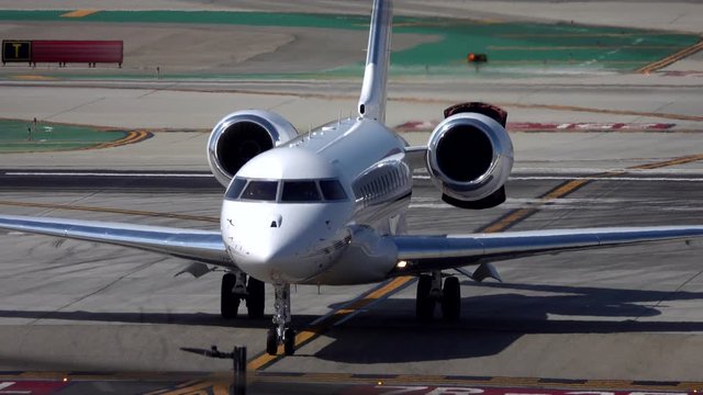 A modern, unmarked business jet taxis at an airport during a summer day.
