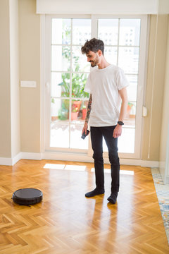 Young man using automatic vacuum cleaner to clean the floor, controling machine housework robot