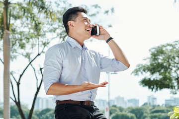 Happy excited Asian entrepreneur actively gesturing when talking on phone outdoors