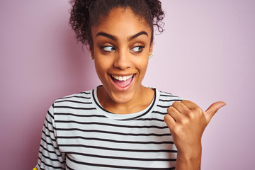 African american woman wearing navy striped t-shirt standing over isolated pink background pointing and showing with thumb up to the side with happy face smiling