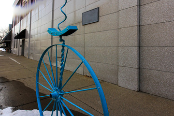 Polished brick exterior wall with plaque. A turqoise unicycle with a curl on the seat.
