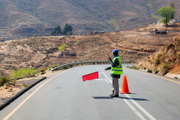 Road worker holds in hand red flag prohibiting traffic, travel restrictions, road repair, customs border transport control, reverse movement, no way sign, limited access symbol, stop movement gesture