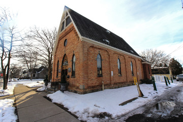 Red brick church with classic windows, blue skies, white clouds, and snow covered ground.
