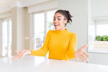 Beautiful african american woman with afro hair wearing a casual yellow sweater smiling cheerful with open arms as friendly welcome, positive and confident greetings