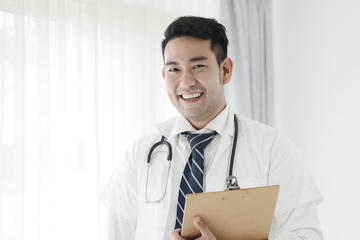 Happy confident Asian doctor standing near window, lifestyle concept.