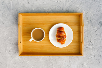Cup of coffee with milk and freshly baked croissant on wooden tray on gray stone table. Concept Good morning Top view