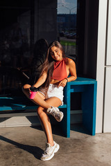 Stylish happy young brunette woman wearing white shorts and sneakers holding pink cup of coffee to go.