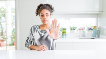 Beautiful african american woman with afro hair wearing casual striped sweater doing stop sing with palm of the hand. Warning expression with negative and serious gesture on the face.