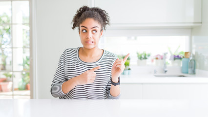 Beautiful african american woman with afro hair wearing casual striped sweater Pointing aside worried and nervous with both hands, concerned and surprised expression