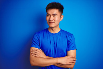 Young asian chinese man wearing t-shirt standing over isolated blue background smiling looking to the side and staring away thinking.