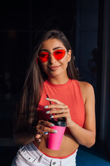 Obraz premium Stylish happy young brunette woman holding pink cup of coffee to go.