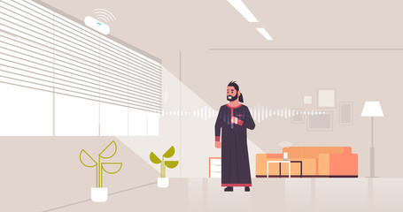arab man using smart speaker voice recognition activated digital assistant concept modern living room interior flat horizontal full length
