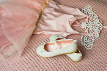 Little shoes and pink dress on a bed in kid bedroom. kid prepare to party. 