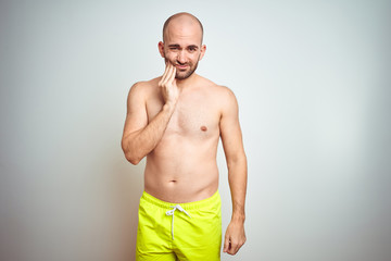 Young shirtless man on vacation wearing yellow swimwear over isolated background touching mouth with hand with painful expression because of toothache or dental illness on teeth. Dentist concept.