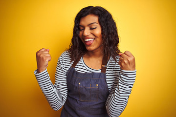 Young transsexual transgender chef woman wearing apron over isolated yellow background very happy and excited doing winner gesture with arms raised, smiling and screaming for success. 