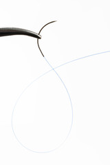 Needle holder with curved needle with blue thread.