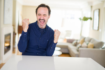 Handsome middle age man at home very happy and excited doing winner gesture with arms raised, smiling and screaming for success. Celebration concept.