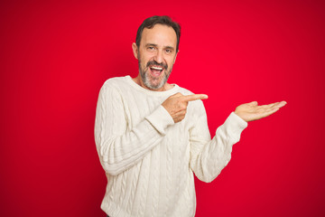 Fototapeta premium Handsome middle age senior man with grey hair over isolated red background amazed and smiling to the camera while presenting with hand and pointing with finger.