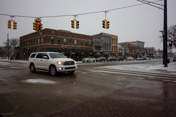 Intersection in a midwesterntown. Street lights on a line from corner to corner. Brick buildings from the early 1900's, with a snow covered ground.