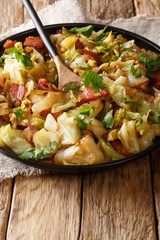 Tasty fried cabbage with crispy bacon closeup on a plate on a table. vertical