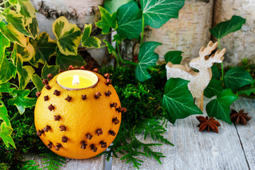 Orange pomander ball with candle on wooden table.