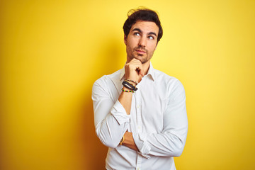 Young handsome businessman wearing elegant shirt standing over isolated yellow background with hand on chin thinking about question, pensive expression. Smiling with thoughtful face. Doubt concept.