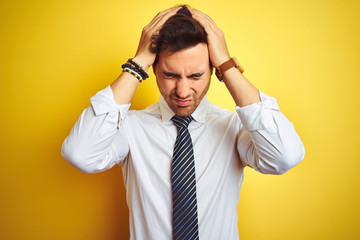 Young handsome businessman wearing elegant shirt and tie over isolated yellow background suffering from headache desperate and stressed because pain and migraine. Hands on head.