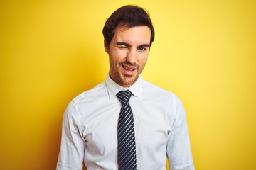Young handsome businessman wearing elegant shirt and tie over isolated yellow background winking looking at the camera with sexy expression, cheerful and happy face.