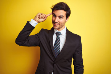 Young handsome businessman wearing suit and tie standing over isolated yellow background Smiling pointing to head with one finger, great idea or thought, good memory