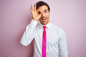 Young handsome businessman wearing shirt and tie standing over isolated pink background doing ok gesture with hand smiling, eye looking through fingers with happy face.