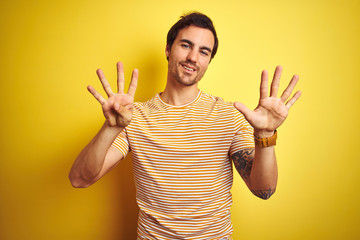 Young handsome man with tattoo wearing striped t-shirt over isolated yellow background showing and...