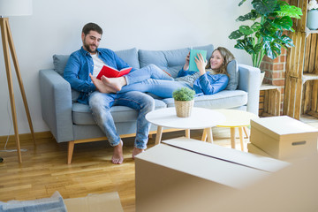 Young couple relaxing on the sofa reading a book, taking a break for moving to new house